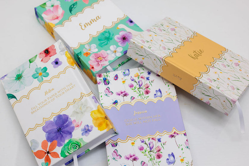 Set of floral notebooks with personalized gold foiled names on a light background