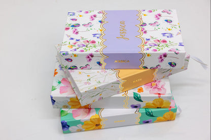 Stack of colorful journal notebooks with floral patterns and custom gold foiled name on a white background